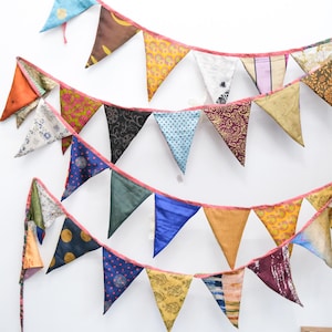 May include: A collection of colorful fabric bunting flags in various patterns and colors, including blue, orange, yellow, and green. The flags are strung together with pink ribbon, creating a festive and decorative display.