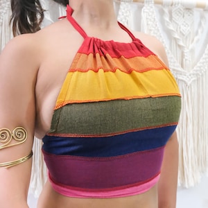 May include: A halter-style crop top featuring horizontal stripes in red, orange, yellow, olive green, blue, purple, and pink. The garment has a gathered neckline with thin straps that tie behind the neck and exposed sides.
