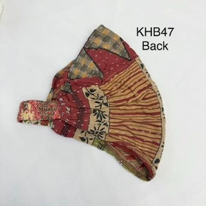 May include: A headband featuring a patchwork design with various patterns in shades of red, tan, and yellow. The fabric displays visible stitching and a gathered elastic section. The text KHB47 Back is printed in black on the upper right side.