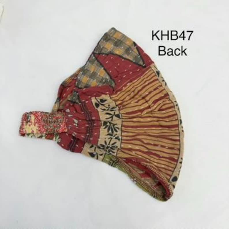 May include: A headband featuring a patchwork design with various patterns in shades of red, tan, and yellow. The fabric displays visible stitching and a gathered elastic section. The text KHB47 Back is printed in black on the upper right side.