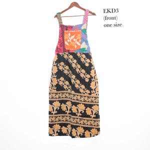 May include: A sleeveless apron dress on a wooden hanger, featuring a black skirt with a tan floral pattern and a multicolored patchwork bodice with an orange pocket. The text EKD3 (front) one size is printed in the upper right corner.