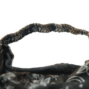 May include: A black fabric headband featuring a white celestial print with stars, moons, and suns. The accessory has an elasticated back section for a secure fit, with gathered fabric detailing along the band and a soft, flexible construction.