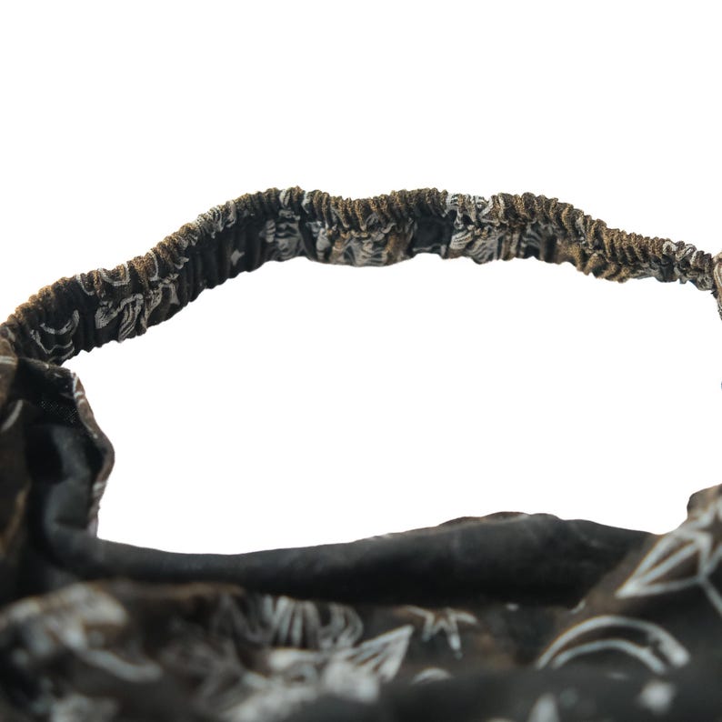 May include: A black fabric headband featuring a white celestial print with stars, moons, and suns. The accessory has an elasticated back section for a secure fit, with gathered fabric detailing along the band and a soft, flexible construction.