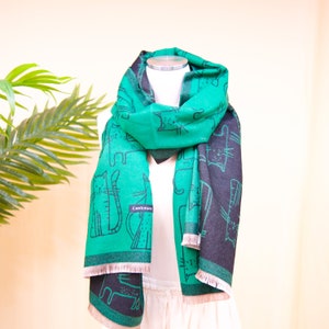 K&ouml;nnte beinhalten: Ein gr&uuml;n-schwarzer Kaschmirschal mit Katzenmuster. Der Schal hat einen Fransenrand und das Wort "Cashmere" ist auf den Schal gedruckt.