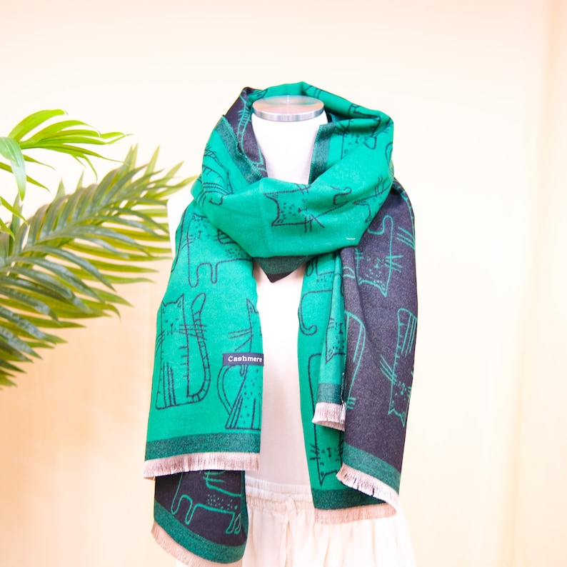 K&ouml;nnte beinhalten: Ein gr&uuml;n-schwarzer Kaschmirschal mit Katzenmuster. Der Schal hat einen Fransenrand und das Wort "Cashmere" ist auf den Schal gedruckt.