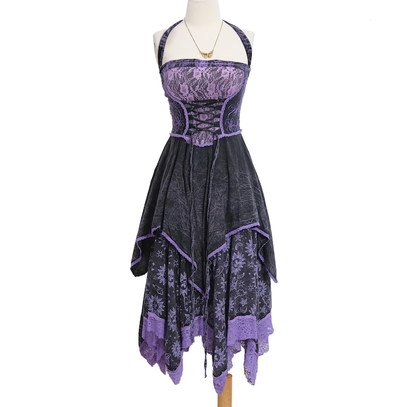 May include: A halter-style dress featuring a black and purple color scheme. The bodice includes a lace overlay and a corset-style lace-up front. The skirt has an asymmetrical handkerchief hemline with a celestial sun and moon print pattern.