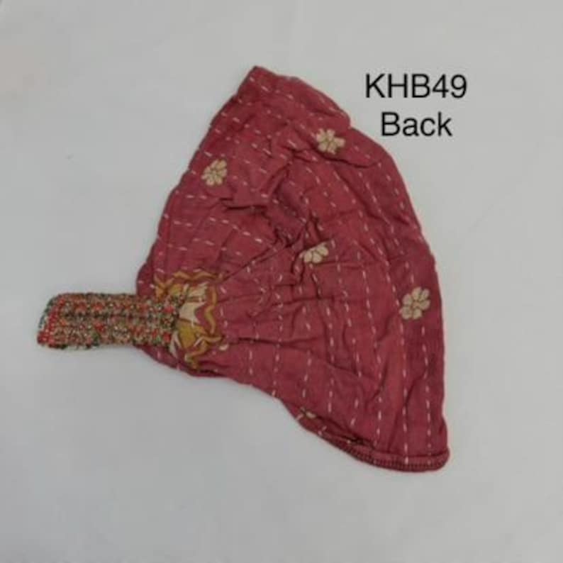 May include: A dusty rose fabric headwrap featuring white dashed vertical stitching and small floral patterns. The accessory includes a multi-colored patterned elastic band at the side. The text KHB49 Back is printed in black in the upper right corner.