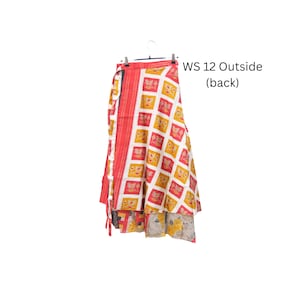 Op de afbeelding: Een wikkelrok met een wit ruitpatroon, gele en rode bloemmotieven en een effen rode verticale rand aan de linkerkant. De tekst WS 12 Outside (back) is zichtbaar. De zoom onthult een tweede laag met een grijs bloemenpatroon.