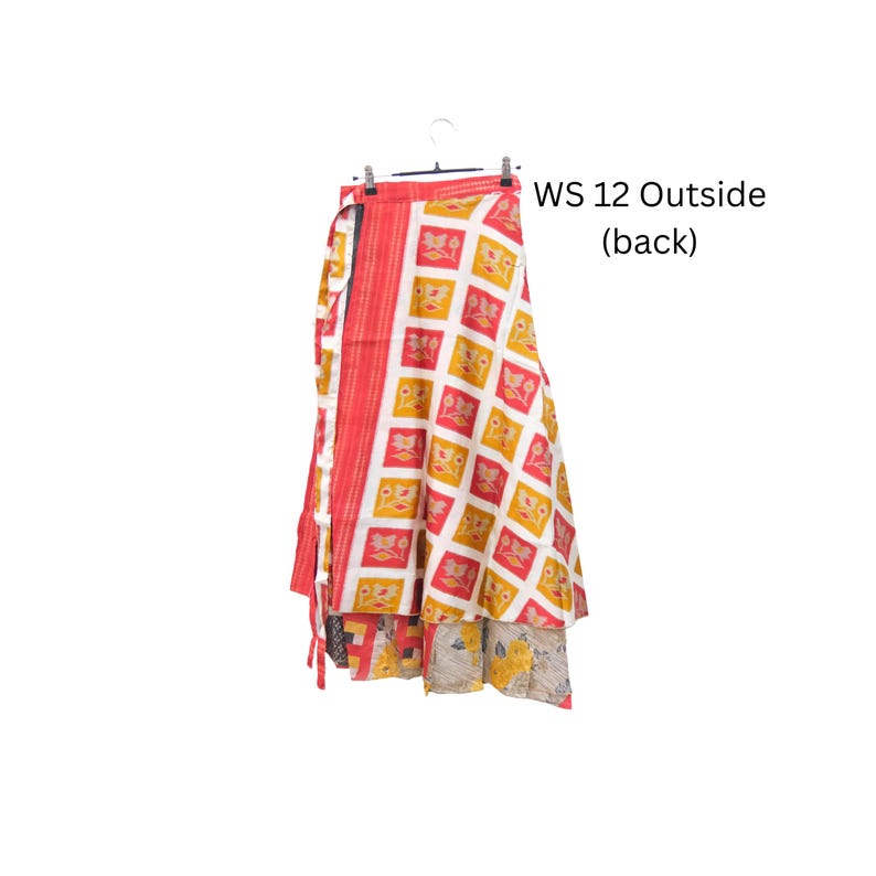 Op de afbeelding: Een wikkelrok met een wit ruitpatroon, gele en rode bloemmotieven en een effen rode verticale rand aan de linkerkant. De tekst WS 12 Outside (back) is zichtbaar. De zoom onthult een tweede laag met een grijs bloemenpatroon.