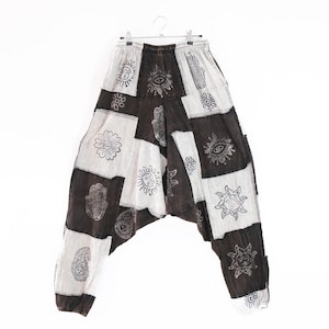 Può includere: Pantaloni dal taglio ampio caratterizzati da un design patchwork con pannelli di tessuto alternati in bianco e nero. Il capo è decorato con stampe nere a inchiostro raffiguranti soli, occhi, mani di hamsa, fiori e motivi cachemire.