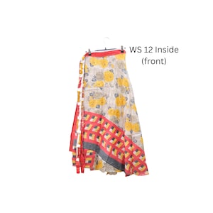Op de afbeelding: Een wikkelrok met een cr&egrave;mekleurige basis, gele bloemenpatronen, een rood-gele geometrische rand en een rode tailleband. De tekst WS 12 Inside (front) is zichtbaar. De rok hangt aan een kledinghanger tegen een witte achtergrond.