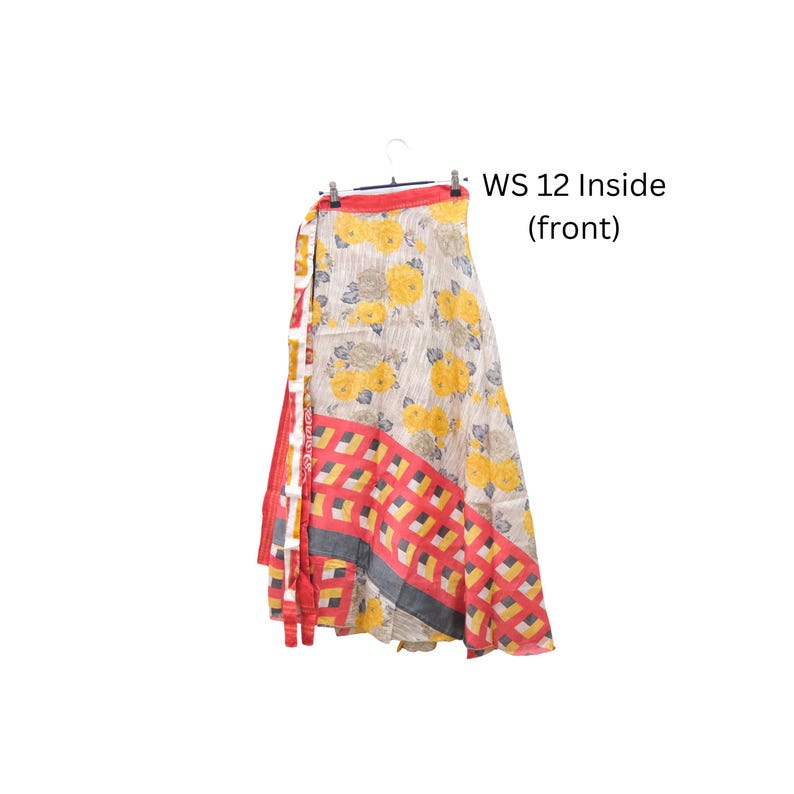Op de afbeelding: Een wikkelrok met een cr&egrave;mekleurige basis, gele bloemenpatronen, een rood-gele geometrische rand en een rode tailleband. De tekst WS 12 Inside (front) is zichtbaar. De rok hangt aan een kledinghanger tegen een witte achtergrond.