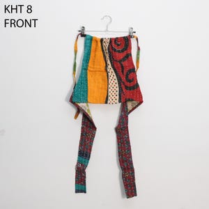 May include: A colorful, patchwork apron with a variety of patterns and colors, including teal, orange, and red. The apron is hanging on a metal hanger against a white background. The text "KHT 8 FRONT" is visible.