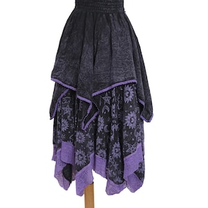 May include: A black midi skirt with a smocked waistband and a layered handkerchief hem. The top layer features a solid acid-wash texture, while the bottom layer displays a purple celestial print of suns, moons, and stars, finished with purple lace trim.
