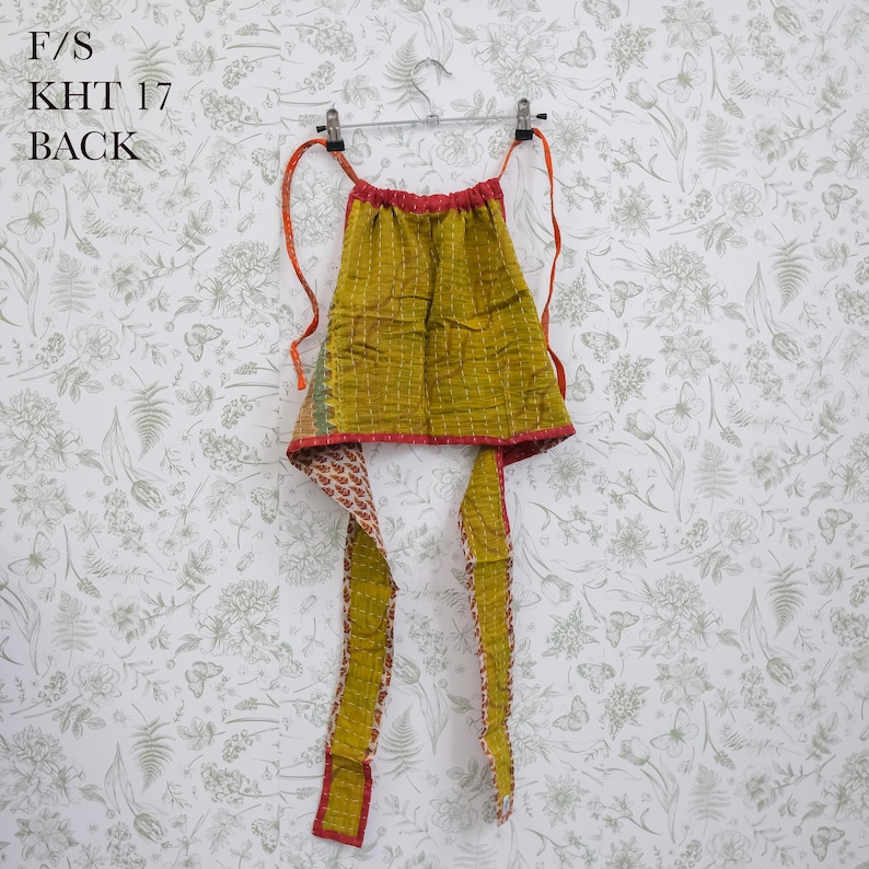 May include: A mustard yellow quilted halter top featuring a grid pattern and red trim, with long fabric ties extending from the top corners. The text F/S KHT 17 BACK is printed in the upper left corner of the image.