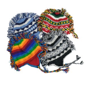 Peut inclure: Quatre bonnets en tricot colorés avec garniture à franges. Les chapeaux présentent divers motifs, notamment des rayures, des zigzags et un motif arc-en-ciel. Chaque chapeau a des cache-oreilles avec des liens tressés.