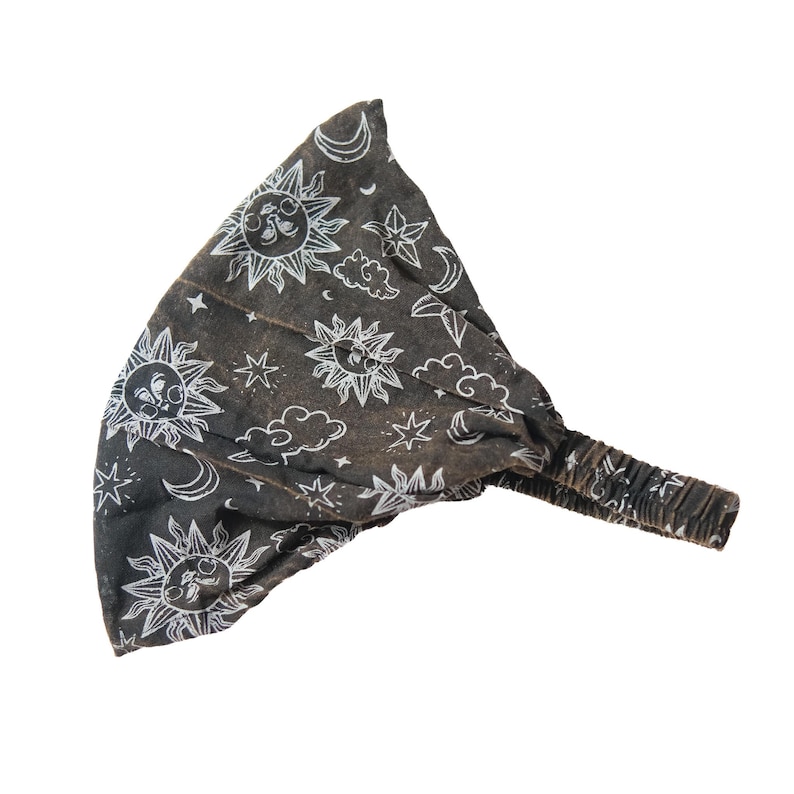 May include: A dark grey fabric headband featuring a white line-art pattern of suns, crescent moons, stars, and clouds. The accessory includes a gathered elastic band section at the back to provide a secure fit for the wearer.