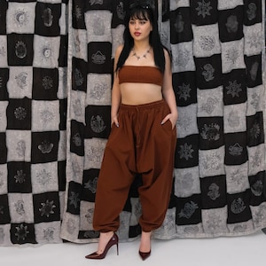 May include: A brown two-piece set consisting of a strapless tube top with a textured finish and matching loose-fitting, high-waisted harem pants featuring an elasticized waistband with a drawstring and side pockets, paired with dark brown high heels.