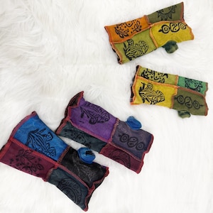 May include: Three pairs of fingerless gloves made from patchwork fabric panels. Each pair features distinct color combinations including orange, green, yellow, blue, purple, and maroon, with black printed botanical and circular graphic designs.