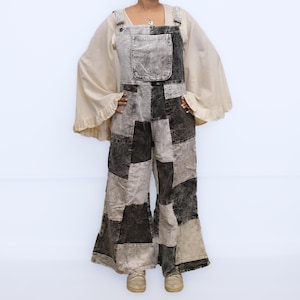 May include: A pair of patchwork overalls featuring a mix of black, charcoal, and light gray corduroy fabric panels. The overalls have a large front chest pocket, wide legs, and are worn over a cream-colored top with long, flared, ruffled sleeves.