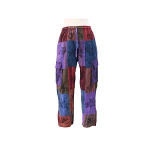 Puede incluir: Pantalones cargo de patchwork con un diseño multicolor de paneles de tela morados, azules, rojos y verdes. Los pantalones incluyen una cintura con cordón, dos bolsillos cargo laterales y un estampado repetido de mariposas negras.