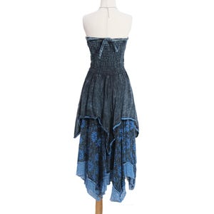 May include: A strapless midi dress in a dark blue acid-wash finish featuring a smocked bodice with a tie-back closure. The skirt has an asymmetrical handkerchief hemline with a layered blue floral print pattern and a light blue lace trim border.