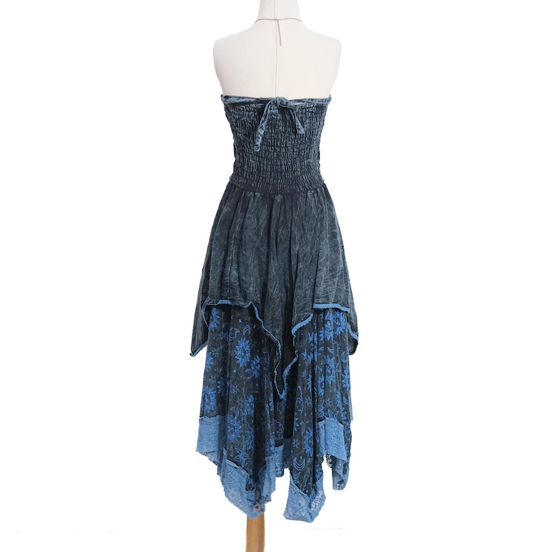 May include: A strapless midi dress in a dark blue acid-wash finish featuring a smocked bodice with a tie-back closure. The skirt has an asymmetrical handkerchief hemline with a layered blue floral print pattern and a light blue lace trim border.