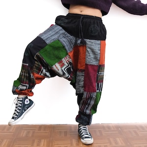 Può includere: Pantaloni alla turca in patchwork con elastico in vita nero e coulisse. I pantaloni sono realizzati con vari pannelli di tessuto nelle tonalità del verde, arancione, bordeaux e nero, che mostrano diversi motivi geometrici e floreali.