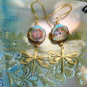 May include: Gold tone earrings with a blue and brown floral bead and a dragonfly charm.