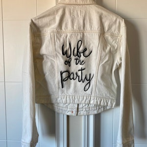 May include: White denim jacket with black embroidery that says "Wife of the Party".