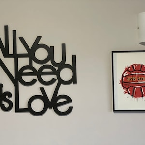 Può includere: Arte da parete nero con le parole "All You Need Is Love" in un font moderno. Una stampa incorniciata di un pallone da calcio rosso con le parole "Super Santos" è sul muro a destra.
