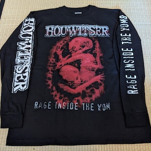 Puede incluir: Camiseta negra de manga larga con un estampado gráfico rojo y blanco de una criatura. El texto "HOOWITSER" está impreso en blanco en la parte delantera de la camiseta. El texto "RAGE INSIDE THE WOMB" está impreso en blanco en las mangas.