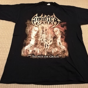 May include: Black t-shirt with a graphic print of two figures in robes, with the band name "FINISTERRE" and the text "SAVAGE OR GRACE" printed below.