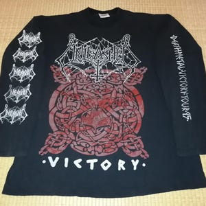 May include: Black long-sleeved shirt with the band name "Unleashed" in white, and a red and white graphic on the front. The sleeves have additional text and graphics. The word "Victory" is printed in white at the bottom of the shirt.