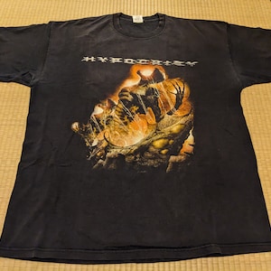 Pode incluir: Camiseta preta com uma estampa gráfica de um monstro com chamas e a palavra "HYPOCRISY" em letras brancas.