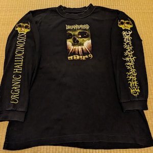 Puede incluir: Camiseta negra de manga larga con un gráfico de calavera y el texto "Dethklok" y "Ways 9" en la parte delantera. Las mangas tienen un gráfico dorado de llamas y una calavera.