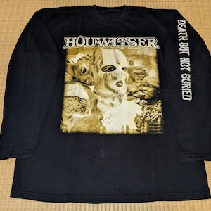 Puede incluir: Camiseta negra de manga larga con un gráfico dorado de una figura enmascarada y el texto "HOUWITZER" y "DEATH BUT NOT BURIED" en la manga.