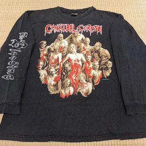 Puede incluir: Camiseta negra de manga larga con un gráfico de figuras con detalles en rojo y el texto "Cannibal Corpse" en rojo. La manga izquierda tiene la palabra "Bleeding" en blanco. La camiseta es de material suave.