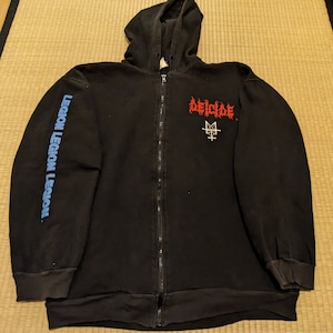 May include: Black zip-up hoodie with the word "DEICIDE" in red and a white graphic on the front. The left sleeve has the words "LEGION LEGION LEGION" in blue. The hoodie has a drawstring hood.