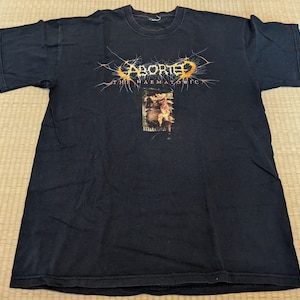 May include: Black t-shirt with a graphic of the band Aborted. The graphic is in orange and yellow and features the band's name and the album title "The Haematologic".