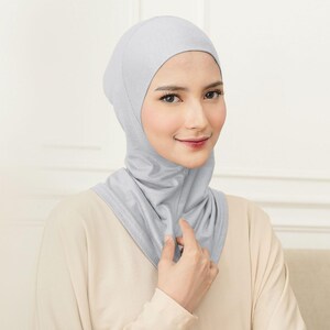 May include: A light gray hijab with a matching neck covering. The head covering is made of a soft, draping fabric. The person in the image is wearing a light beige top.
