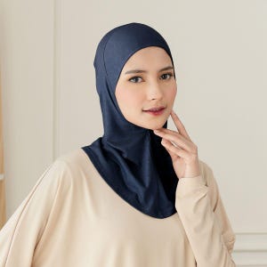 May include: A navy blue hijab, a head covering, is worn by a person. The hijab is made of a soft fabric and covers the head and neck. The person is wearing a light beige top.