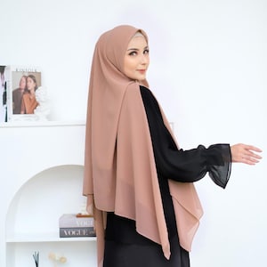 Könnte beinhalten: Eine Frau trägt einen langen, fließenden, hellbraunen Hijab mit einem schwarzen Oberteil und langen Ärmeln. Der Hijab ist über ihre Schultern gelegt und fällt bis zur Taille.