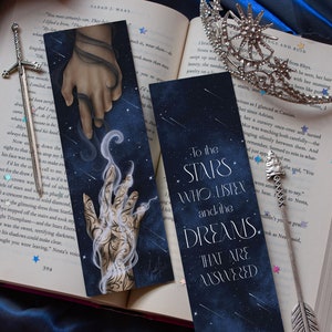 May include: Two bookmarks with a dark blue background and white stars. The text on the bookmarks reads "To the Stars Who Listen and the Dreams That Are Answered".