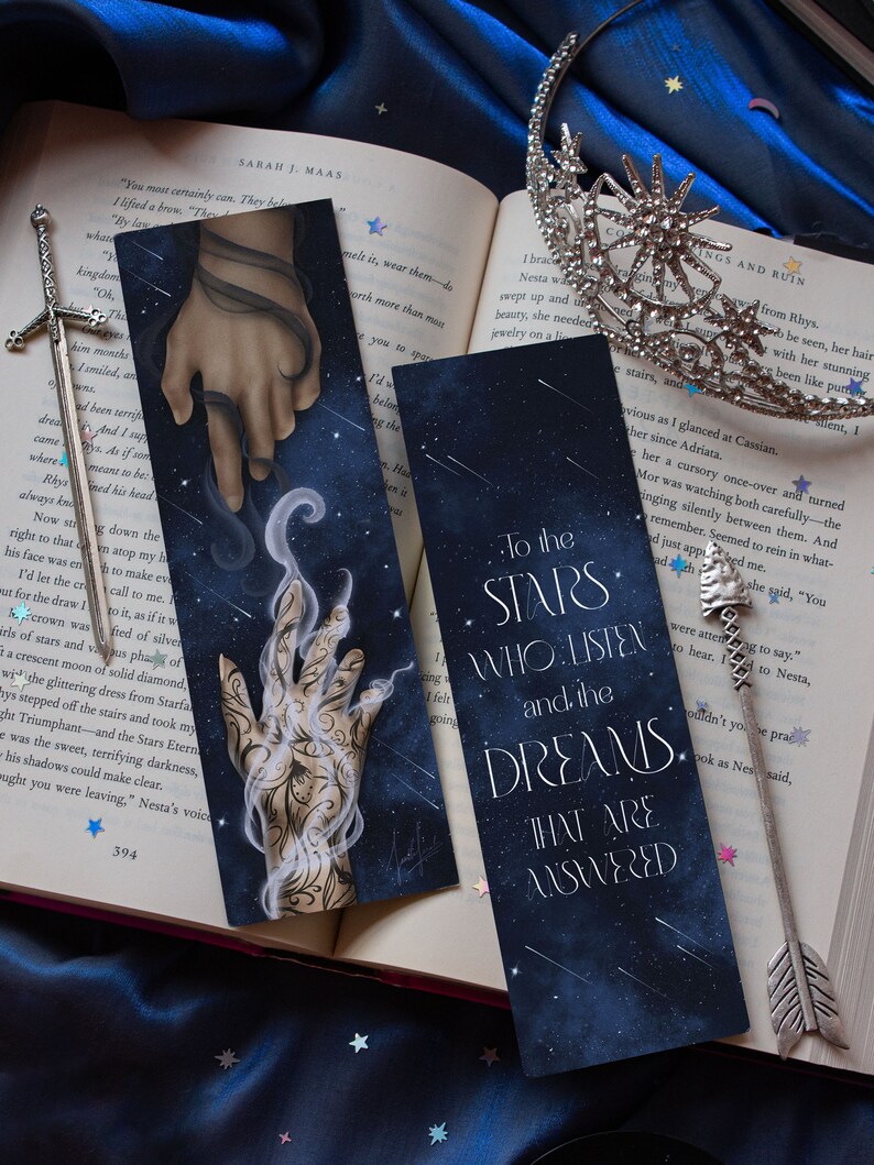 May include: Two bookmarks with a dark blue background and white stars. The text on the bookmarks reads "To the Stars Who Listen and the Dreams That Are Answered".