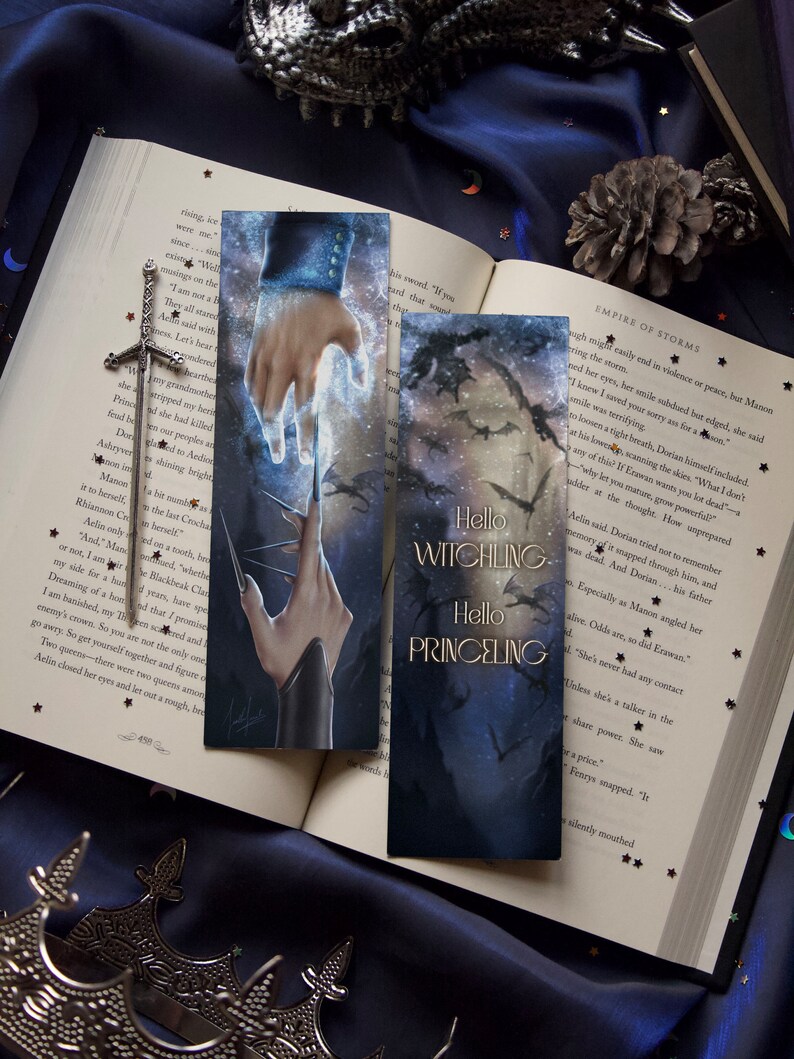 Op de afbeelding: Twee bladwijzers met een fantasie thema. De eerste bladwijzer toont een hand die met een gloeiend licht reikt. De tweede bladwijzer toont een donker bos met een silhouet van een draak en de tekst "Hello Witchling Hello Princeing".