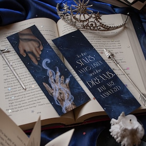 May include: Two blue and black bookmarks with a starry night sky background. One bookmark features a hand reaching out from the sky with the text "To the stars who listen and the dreams that are answered". The other bookmark features a hand reaching out from the sky with a blue and white design.