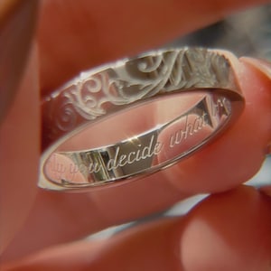 May include: A silver-toned metal ring featuring an intricate, embossed scrollwork pattern on the outer band. The inner surface of the ring is engraved with the cursive text, "only you decide what is". The band has a polished, reflective finish.