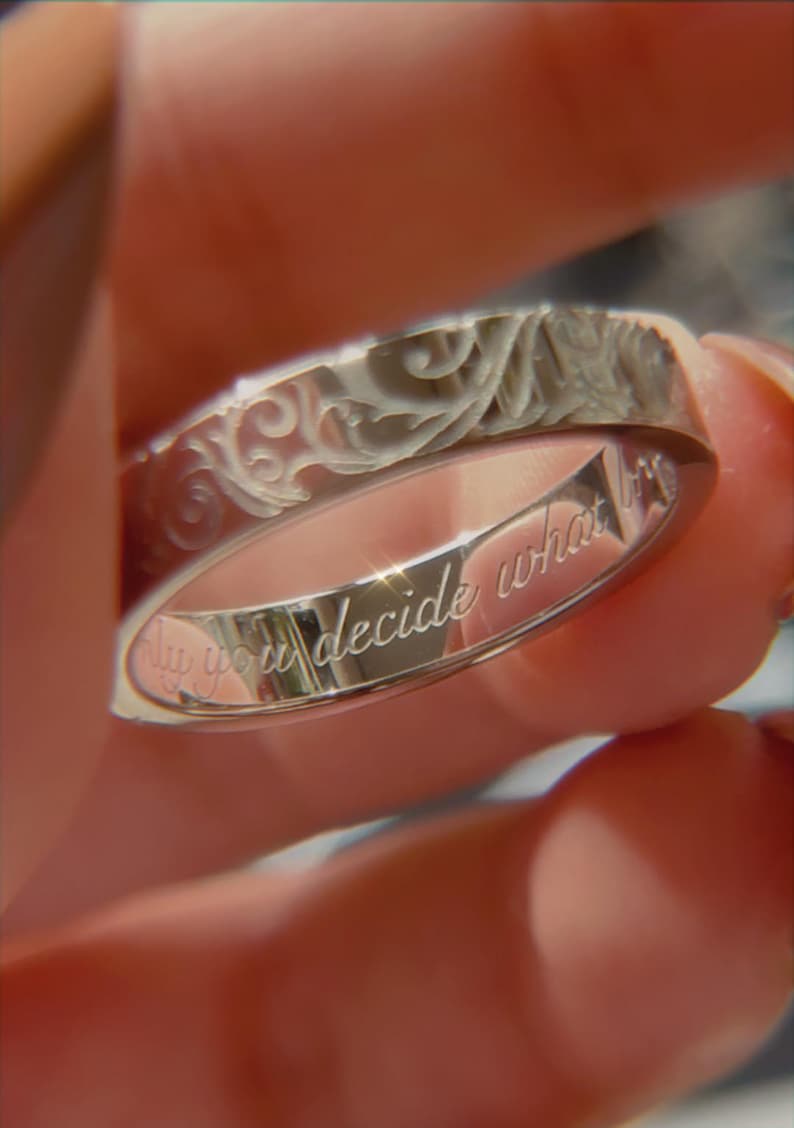 May include: A silver-toned metal ring featuring an intricate, embossed scrollwork pattern on the outer band. The inner surface of the ring is engraved with the cursive text, "only you decide what is". The band has a polished, reflective finish.