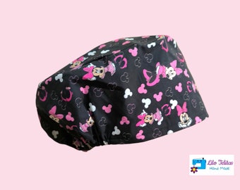 Può includere: Un cappello da lavoro nero con una stampa di Minnie Mouse rosa e bianca. Il cappello ha un elastico bianco ed è fatto di cotone.